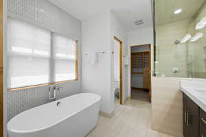 Bathroom featuring a freestanding bath, vanity, a spacious closet, and tiled shower