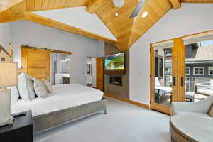 Bedroom featuring carpet flooring, a wood ceiling with exposed beams, high vaulted ceiling, a barn door, and a glass covered fireplace