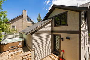 Back of house with a hot tub, a shingled roof, and a chimney