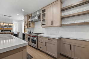 Kitchen featuring wall chimney exhaust hood, stainless steel appliances, light wood-style floors, light countertops, and recessed lighting