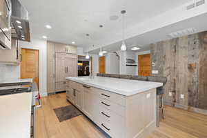 Kitchen with stainless steel gas range, light wood-type flooring, a kitchen breakfast bar, recessed lighting, and wall chimney exhaust hood