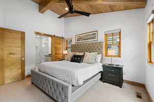 Carpeted bedroom featuring a wooden ceiling with exposed beams, high vaulted ceiling, a barn door, connected bathroom, and a ceiling fan