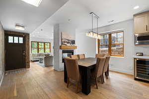 Dining room with recessed lighting, wine cooler, light wood finished floors, a large fireplace, and a chandelier