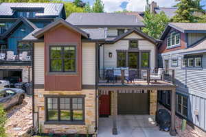 Back of property featuring stone siding, a balcony, concrete driveway, a garage, and roof with shingles
