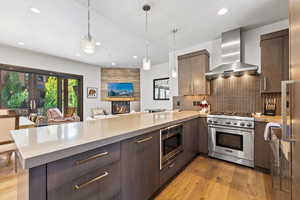 Kitchen with light wood finished floors, a peninsula, appliances with stainless steel finishes, modern cabinets, and wall chimney exhaust hood