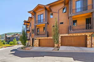 View of front facade with a garage, concrete driveway, stone siding, and a balcony