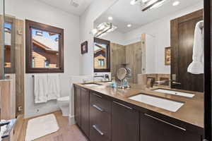 Bathroom featuring double vanity, wood finished floors, tiled shower, and recessed lighting