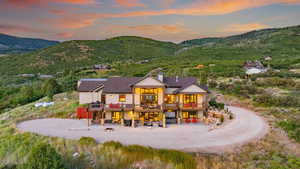 Back of property featuring a fire pit, a chimney, a deck with mountain view, driveway, and roof with shingles