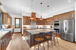 Kitchen with stainless steel appliances, light wood finished floors, a kitchen island with sink, a kitchen breakfast bar, and recessed lighting