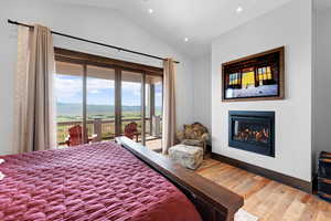 Bedroom with access to outside, lofted ceiling, wood finished floors, a glass covered fireplace, and a mountain view