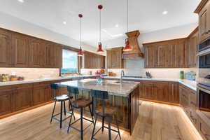 Kitchen featuring tasteful backsplash, a kitchen bar, light wood-style flooring, an island with sink, and double oven
