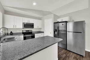 Kitchen with stainless steel appliances, white cabinets, dark wood-style floors, dark stone counters, and vaulted ceiling