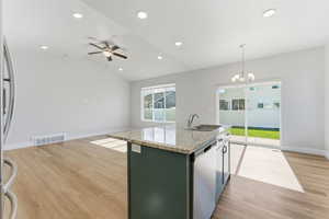 Kitchen featuring light stone counters, a kitchen island with sink, hanging light fixtures, light wood finished floors, and vaulted ceiling