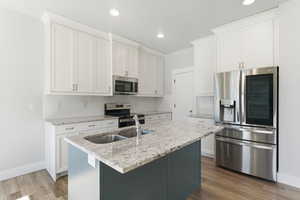 Kitchen with appliances with stainless steel finishes, white cabinets, tasteful backsplash, light stone countertops, and a center island with sink