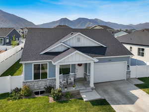 View of front of house with stone siding, covered porch, board and batten siding, roof with shingles, and an attached garage