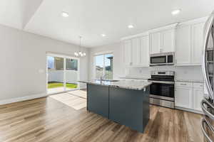 Kitchen featuring stainless steel appliances, white cabinets, decorative light fixtures, light stone countertops, and recessed lighting