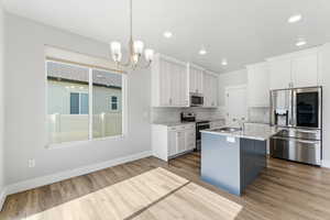 Kitchen featuring stainless steel appliances, white cabinetry, pendant lighting, an island with sink, and a chandelier