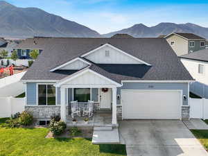 View of front of home with stone siding, covered porch, board and batten siding, and roof with shingles