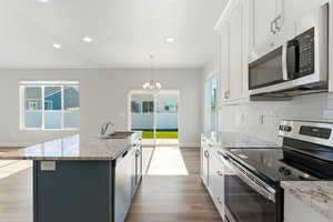 Kitchen with stainless steel appliances, light stone counters, light wood finished floors, white cabinets, and recessed lighting