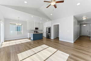 Kitchen with open floor plan, hanging light fixtures, white cabinetry, stainless steel appliances, and vaulted ceiling