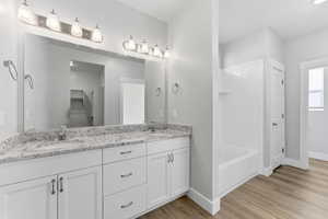Full bathroom featuring double vanity, light wood finished floors, and a spacious closet