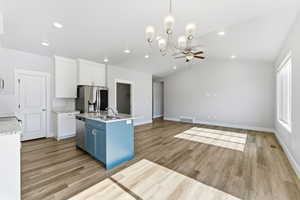Kitchen featuring white cabinets, decorative light fixtures, light stone countertops, appliances with stainless steel finishes, and lofted ceiling
