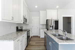 Kitchen with appliances with stainless steel finishes, white cabinets, light stone countertops, dark wood finished floors, and decorative backsplash
