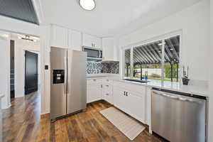 Kitchen with stainless steel appliances, light countertops, decorative backsplash, dark wood-style flooring, and white cabinetry