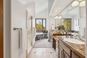 Bathroom featuring lofted ceiling, a bath, healthy amount of natural light, double vanity, and a stall shower