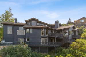 Rear view of property featuring a chimney, a balcony, and a wooden deck