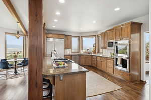 Kitchen with built in appliances, backsplash, brown cabinetry, dark wood-type flooring, and recessed lighting