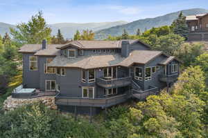 Rear view of house with a chimney, a mountain view, a shingled roof, a balcony, and a hot tub