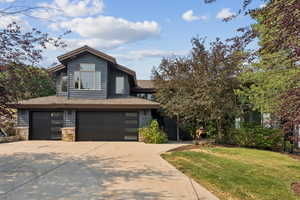 View of front of property with concrete driveway, an attached garage, a front lawn, stone siding, and roof with shingles