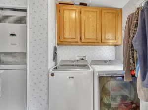 Laundry room with wallpapered walls, separate washer and dryer, a heating unit, and cabinet space