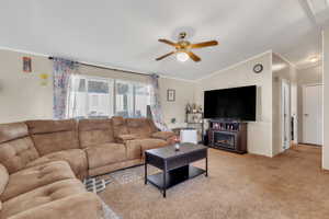 Living area featuring a ceiling fan, crown molding, light colored carpet, vaulted ceiling, and a fireplace