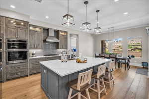 Kitchen featuring backsplash, light wood-style floors, an island with sink, recessed lighting, and stainless steel double oven