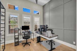 Office with wood finished floors, a decorative wall, and a towering ceiling