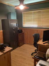 Home office featuring a ceiling fan, light wood-style floors, a wainscoted wall, and wood walls