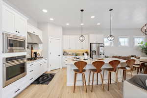 Kitchen with stainless steel appliances, recessed lighting, white cabinets, a kitchen breakfast bar, and light wood-style flooring