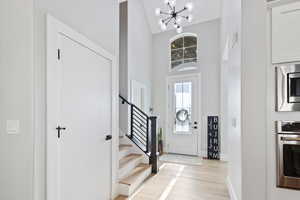 Foyer featuring light wood-style flooring, a chandelier, stairs, and a high ceiling