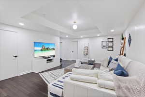 Living room with dark wood-style flooring, recessed lighting, and a tray ceiling