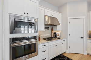 Kitchen featuring appliances with stainless steel finishes, decorative backsplash, light wood finished floors, white cabinets, and under cabinet range hood