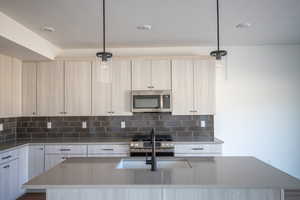 Kitchen featuring light stone countertops, an island with sink, decorative light fixtures, stainless steel appliances, and backsplash