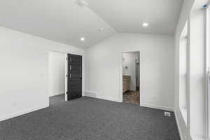 Unfurnished bedroom with dark colored carpet, vaulted ceiling, recessed lighting, and ensuite bathroom