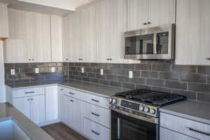 Kitchen with stainless steel appliances, backsplash, light stone counters, and modern cabinets