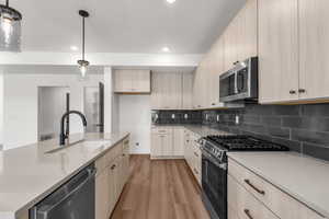 Kitchen featuring light brown cabinets, stainless steel appliances, light wood-style flooring, light countertops, and tasteful backsplash