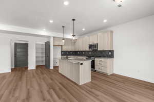 Kitchen featuring light brown cabinetry, a kitchen island with sink, light wood finished floors, light countertops, and stainless steel appliances