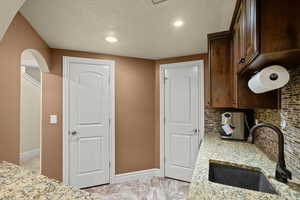 Kitchen with a textured ceiling, light stone countertops, recessed lighting, tasteful backsplash, and dark brown cabinets