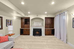 Living room featuring recessed lighting, a textured ceiling, light colored carpet, and a warm lit fireplace
