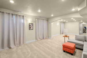 Living area with arched walkways, a textured ceiling, light carpet, and recessed lighting